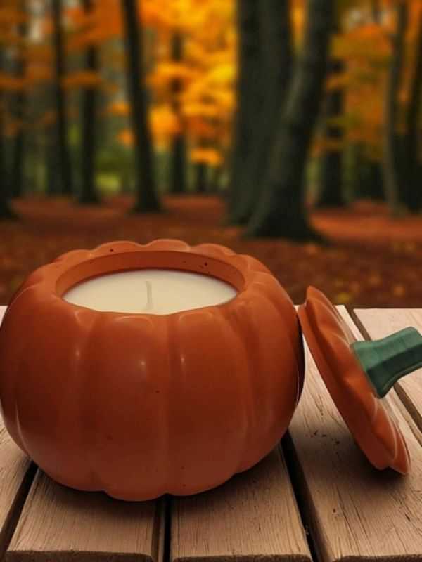 Pumpkin-shaped candle on a table with a blurred autumn forest background.