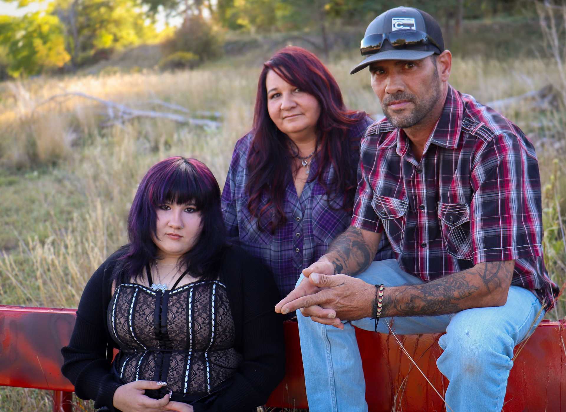 A family outdoors, two women and one man, sitting together in a rustic setting.