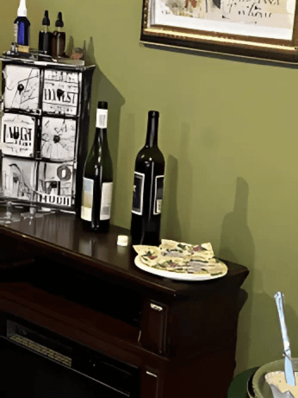 Two wine bottles on a wooden shelf with art and decorative items nearby.