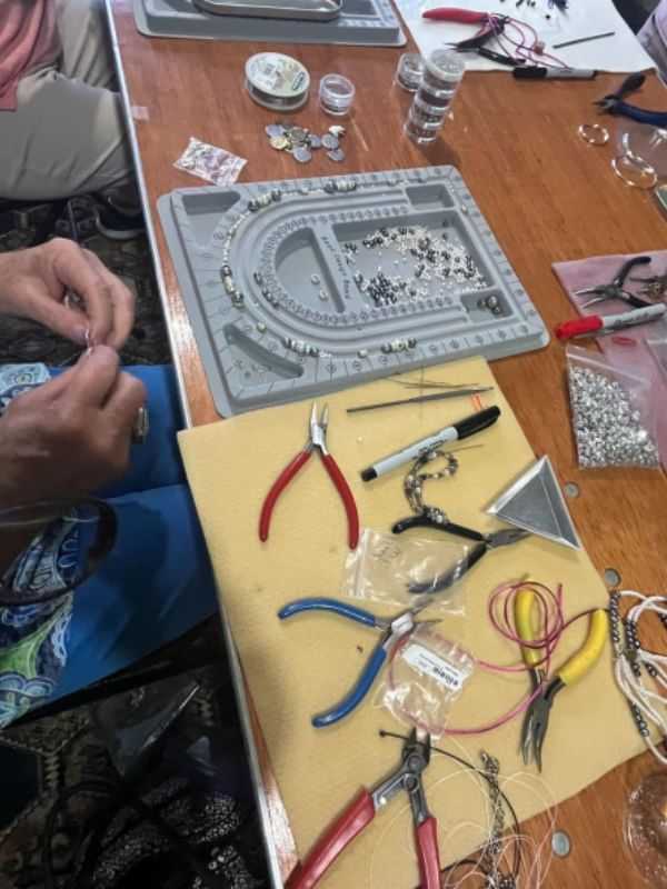 Jewelry-making table with beads, tools, and a necklace in progress.